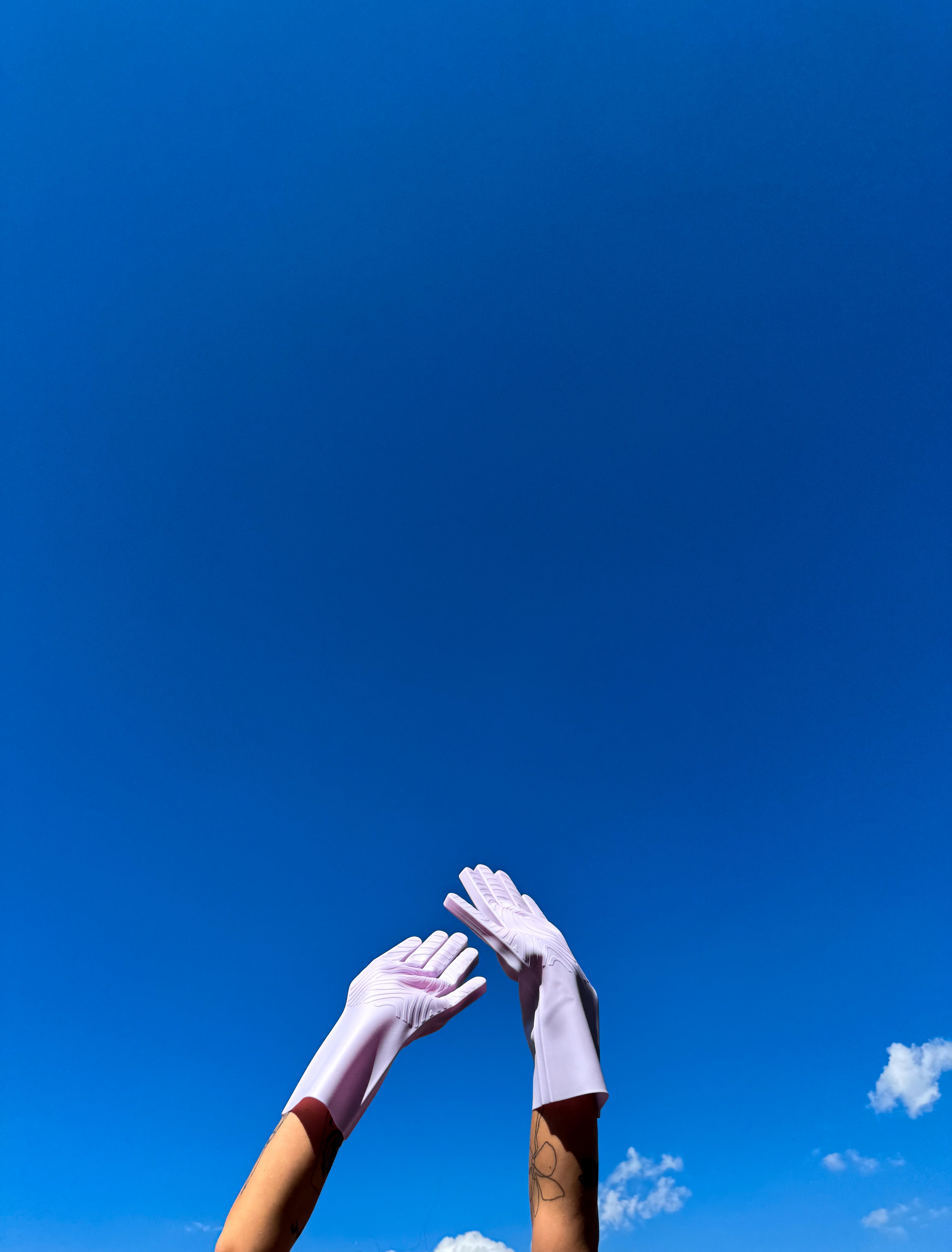 Two hands wearing keeps moondust gloves reaching towards a clear blue sky with a few clouds.