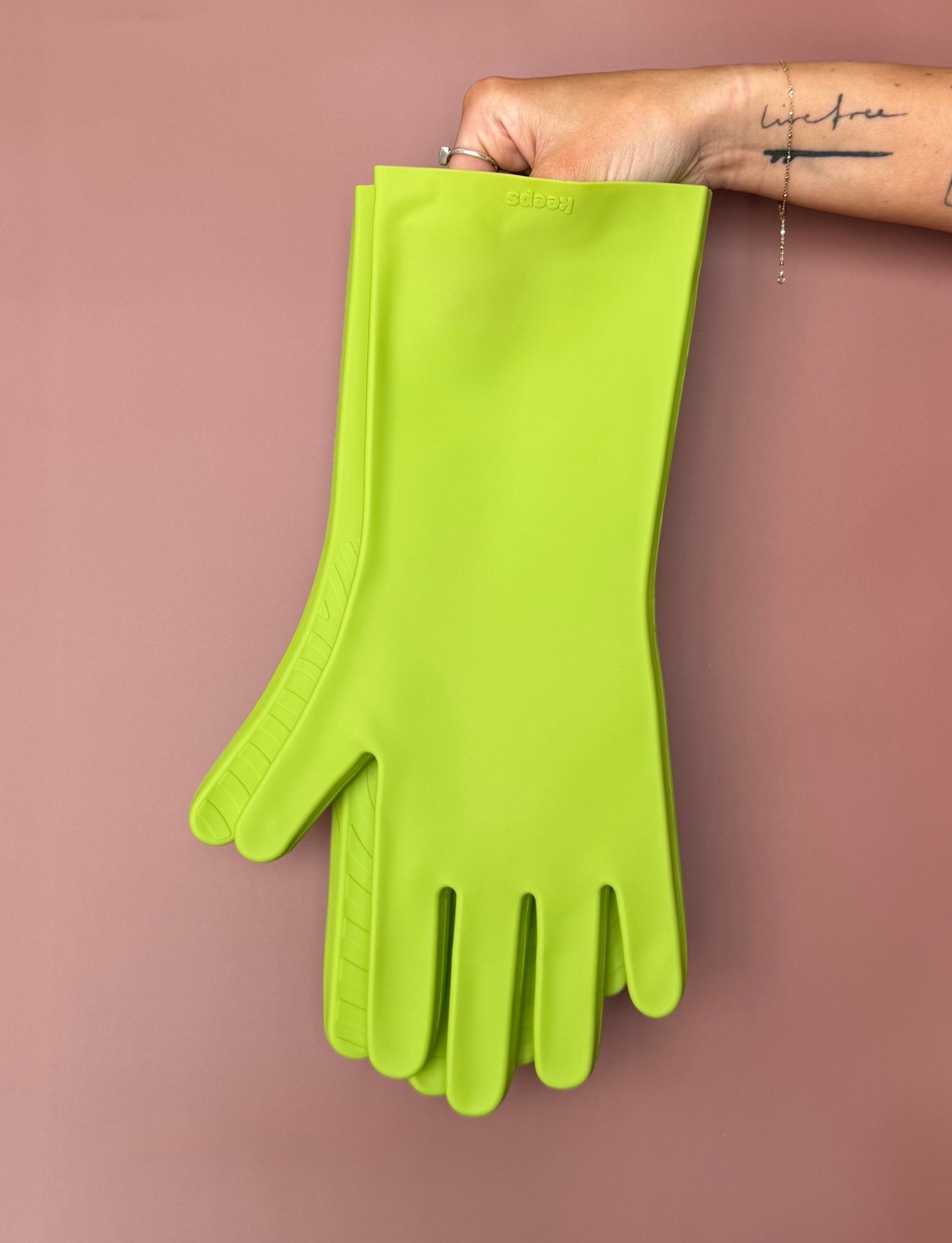keeps gloves in the atomic green colorway held up with bare hands against a terracotta color backdrop