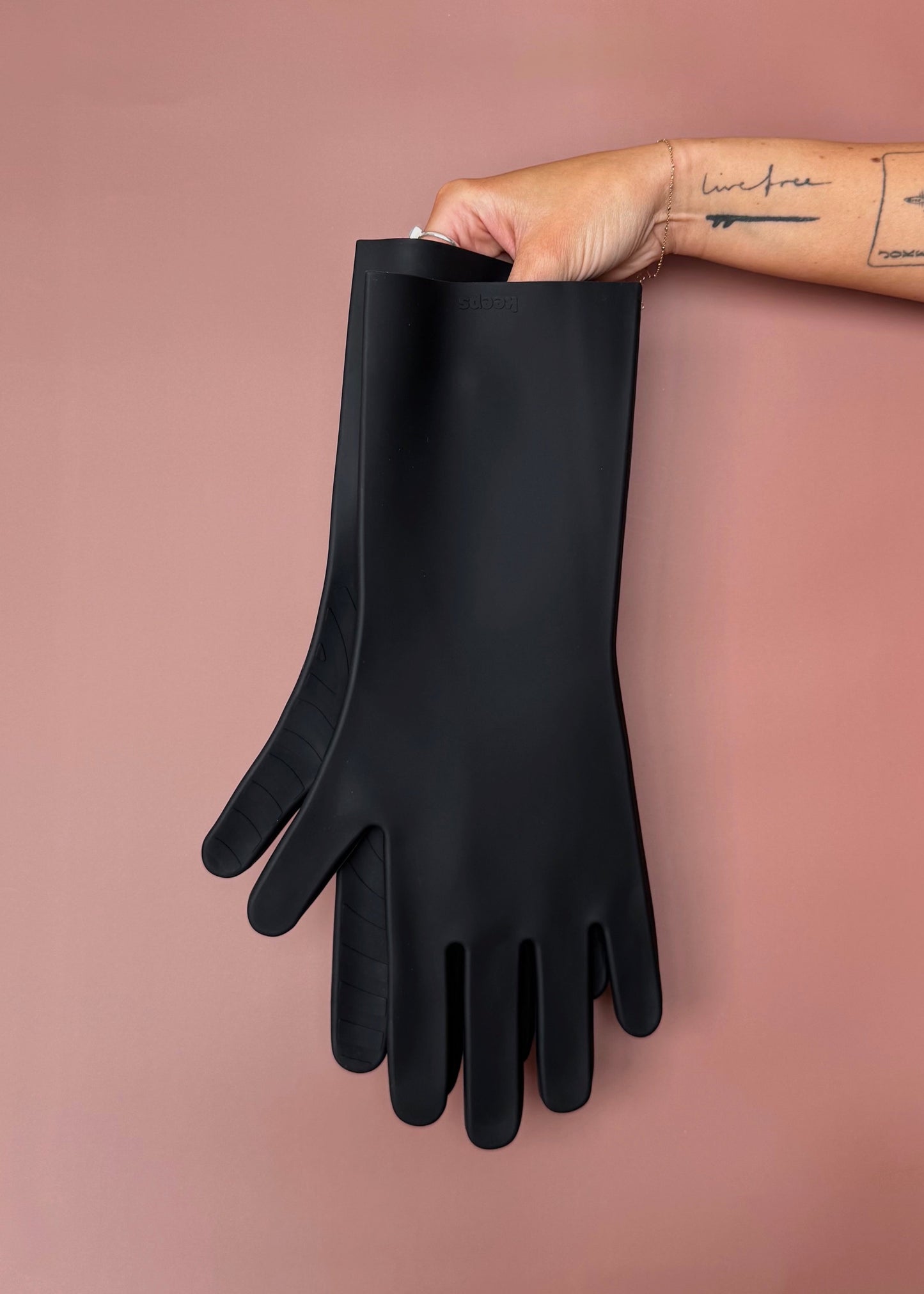 keeps gloves in the black colorway held up with bare hands against a terracotta color backdrop