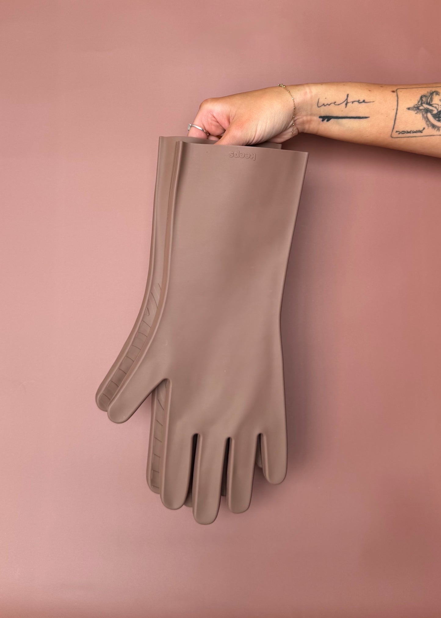keeps gloves in the umber colorway held up with bare hands against a terracotta color backdrop