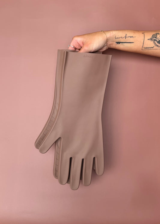 keeps gloves in the umber colorway held up with bare hands against a terracotta color backdrop