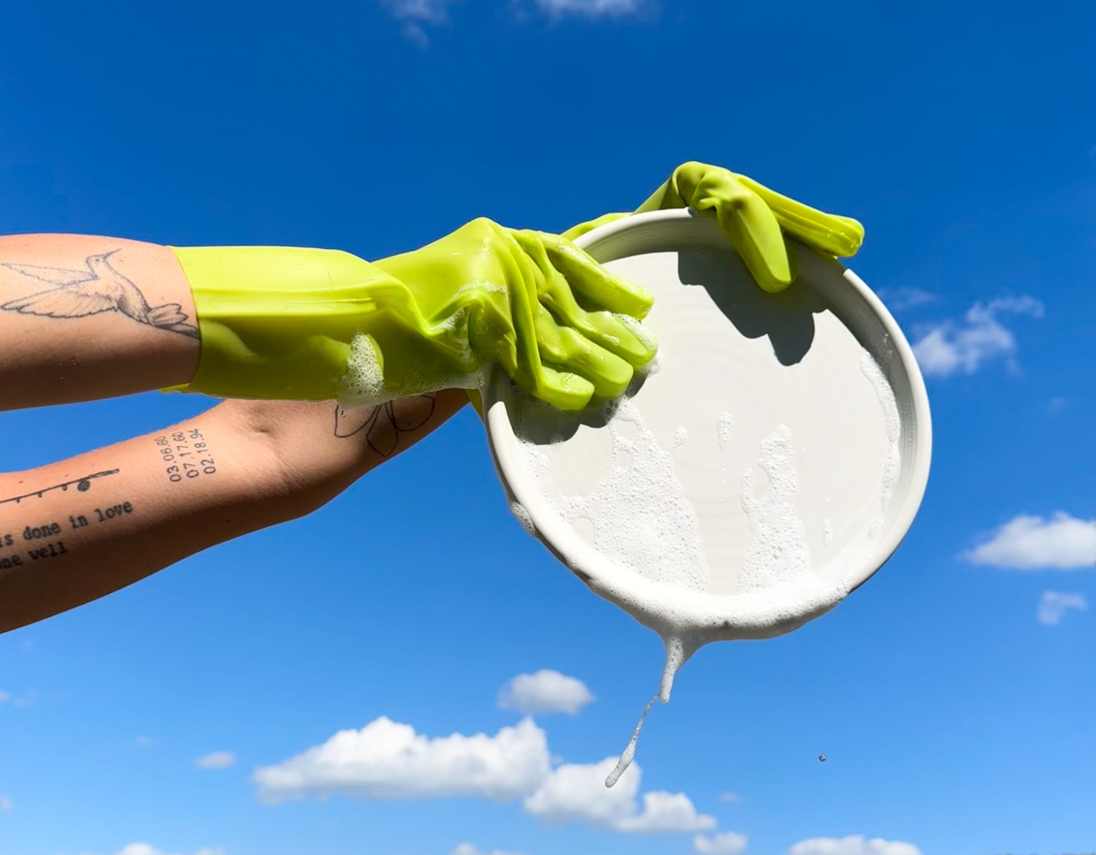 Hand model wearing keeps atomic gloves holding a white plate against a blue sky with clouds