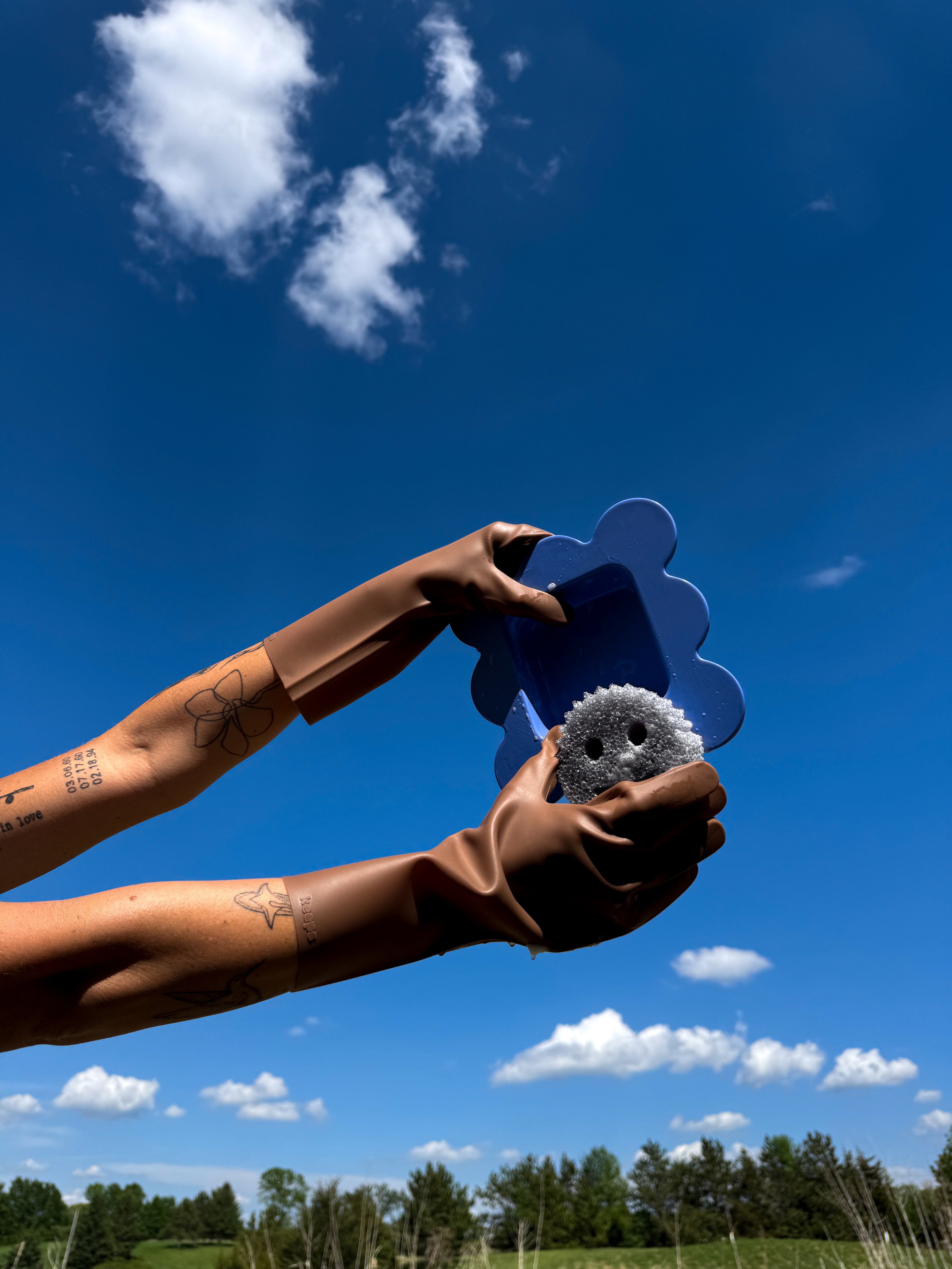 Two hands holding a blue flower bowl in keeps umber brown cleaning gloves against a clear blue sky with white clouds.